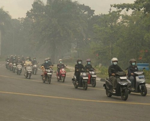 Berkendara motor saat jalan diselimuti kabut asap.