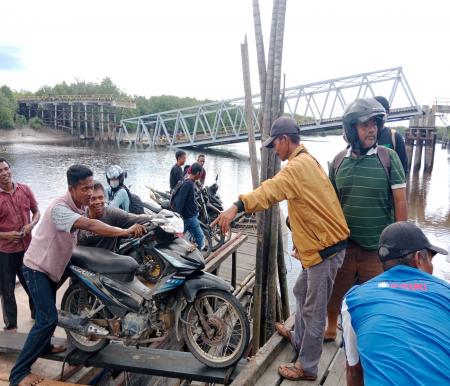 Terlihat warga menyeberangkan sepeda motor menggunakan kapal di sebelah jembatan yang ambruk